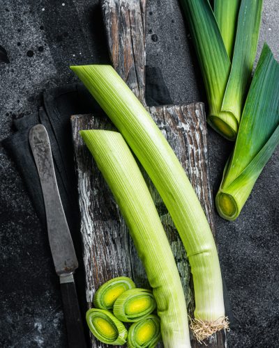 Fresh Raw Green Leeks on wooden cutting board. Black background. Top view.