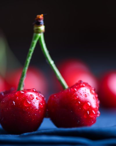Macro shot of two cherries with water droplets on blue napkin on dark background. Food photography